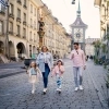 A family strolls through the old town of Bern in the sunshine and eats ice cream.