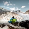 A couple sits on a rock in front of a glacier.