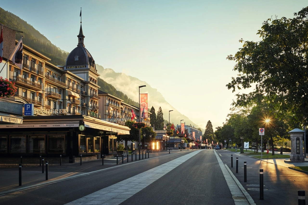 Breite Strasse mit historischen Gebäuden und Bergen im Hintergrund bei Sonnenuntergang.