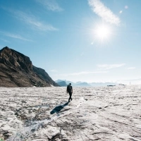 A hiker on a sunny glacier with mountains in the background.