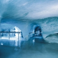 Eine beleuchtete Eishöhle mit glatten, blauen Wänden und einem Durchgang.