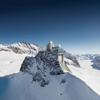 Eine Forschungsstation auf einem schneebedeckten Berggipfel unter blauem Himmel.