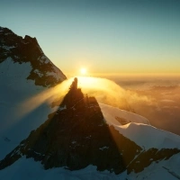 Sunset behind a snow-capped mountain peak with fog.