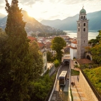 A city view at sunrise with mountains, a church tower, and a mountain railway.