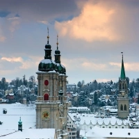 A snowy cityscape with two church towers under a cloudy sky.