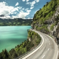 Une route sinueuse au bord d'un lac turquoise, entourée de montagnes et de forêt.