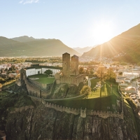 Eine alte Burg auf einem Hügel mit zwei Türmen, umgeben von einer modernen Stadtlandschaft bei Sonnenuntergang.