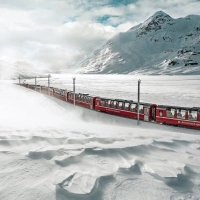 Un treno rosso attraversa un paesaggio montano innevato.