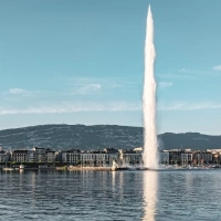 A large water fountain rises in front of a skyline with mountains in the background.