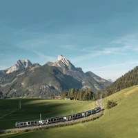 Train passes through green hills in front of a mountainous landscape.
