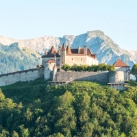 Un château sur une colline, entouré d'arbres verts et de montagnes en arrière-plan.