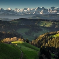 A vast mountain landscape with green hills and snow-capped peaks in the background.