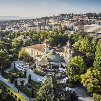 Aerial view of a historic building with a garden, surrounded by trees and a city in the background.