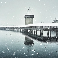 Eine verschneite Holzbrücke mit einem Turm, die über einen Fluss verläuft.