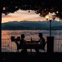 Two people sitting at a table by the lakeside at sunset.