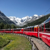 Ein roter Bernina Express Zug fährt durch eine alpine Landschaft mit schneebedeckten Bergen im Hintergrund.