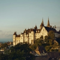 Un château sur une colline, entouré de vieilles maisons, surplombant un lac au coucher du soleil.