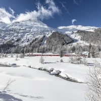 A red train travels through a snowy mountain landscape with a clear sky.