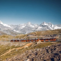 A red train travels through the mountain landscape in front of the Matterhorn.