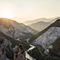 Sunset over a mountain gorge with a river and wooded slopes.