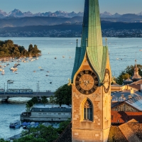 A church with a clock tower, view of the lake with boats and mountains in the background.