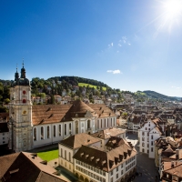 Blick auf eine historische Stadt mit einer grossen Kirche und Hügeln im Hintergrund bei Sonnenschein.