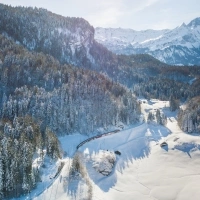 A winter mountain landscape with a train passing through snow-covered forests.