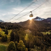 Seilbahn über bewaldeter Berglandschaft mit schneebedecktem Gipfel im Hintergrund.