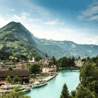 Vue de la ville avec rivière, bateaux et montagnes environnantes en arrière-plan.