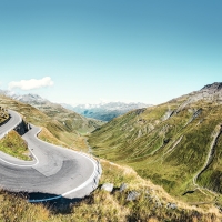 Windy mountain road in a green, hilly landscape under a clear, blue sky.