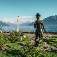 Una statua in un giardino che si affaccia su un lago e montagne, con una grande forchetta in lontananza.