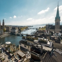 Blick auf Zürich mit Kirche, Fluss und Brücke bei sonnigem Wetter.