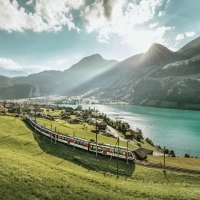 An idyllic mountain landscape with a train passing by a lake.