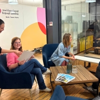 A group of four people sitting together in a modern office looking at a catalog.