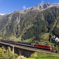 A red locomotive on a viaduct in front of a mountain landscape.