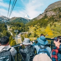 Die Gruppe fährt mit einer Bergbahn mit offenem Deck, im Vordergrund eine Grüne Landschaft und das Matterhorn.