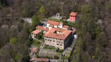 Vue aérienne d'un complexe de bâtiments historiques avec des toits en tuiles rouges dans une zone boisée.