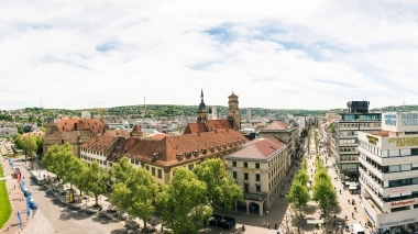 Panoramablick auf eine Stadt mit historischen Gebäuden, Grünflächen und einer belebten Einkaufsstrasse.