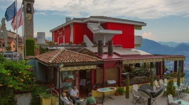 A terrace with tables and chairs, in the background a red building and a church tower.