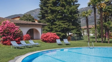 Area piscina rilassata con lettini, fiori colorati e vista sulle montagne.