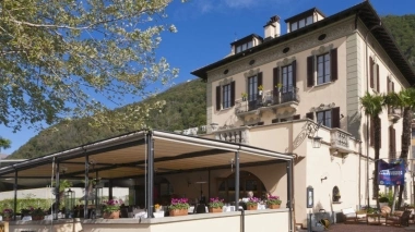 Una villa elegante con grandi finestre e un'area esterna coperta, circondata da colline verdi e cielo limpido.