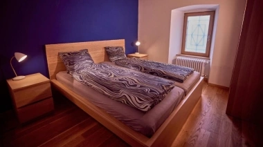 Camera da letto moderna con pavimento in legno, parete dipinta di blu, letto matrimoniale e comodini con lampade.