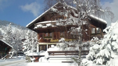 Alpines Holzhaus umgeben von verschneiten Bäumen und Bergen.