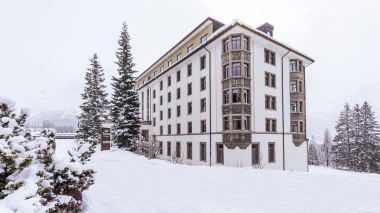 A large white building surrounded by snowy trees and landscape.