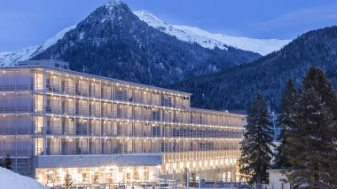 Un bâtiment moderne éclairé devant une toile de fond de montagnes enneigées.