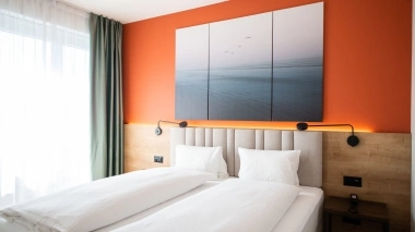 Two single beds in a room with an orange wall and a large mural.