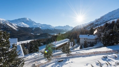 A winter mountain landscape with deeply snow-covered trees and houses, the sun shining in the clear sky.