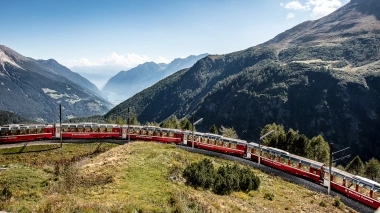 Eine rote Bahn fährt durch eine Gebirgslandschaft.