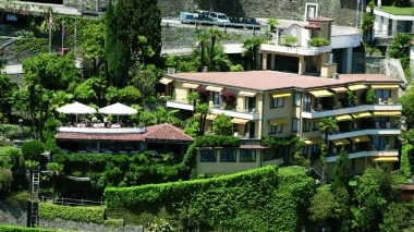 Multistory building on a hill, surrounded by lush greenery and a terrace area with parasols.