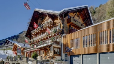 Un chalet suisse traditionnel avec des drapeaux rouges, téléphérique en arrière-plan.